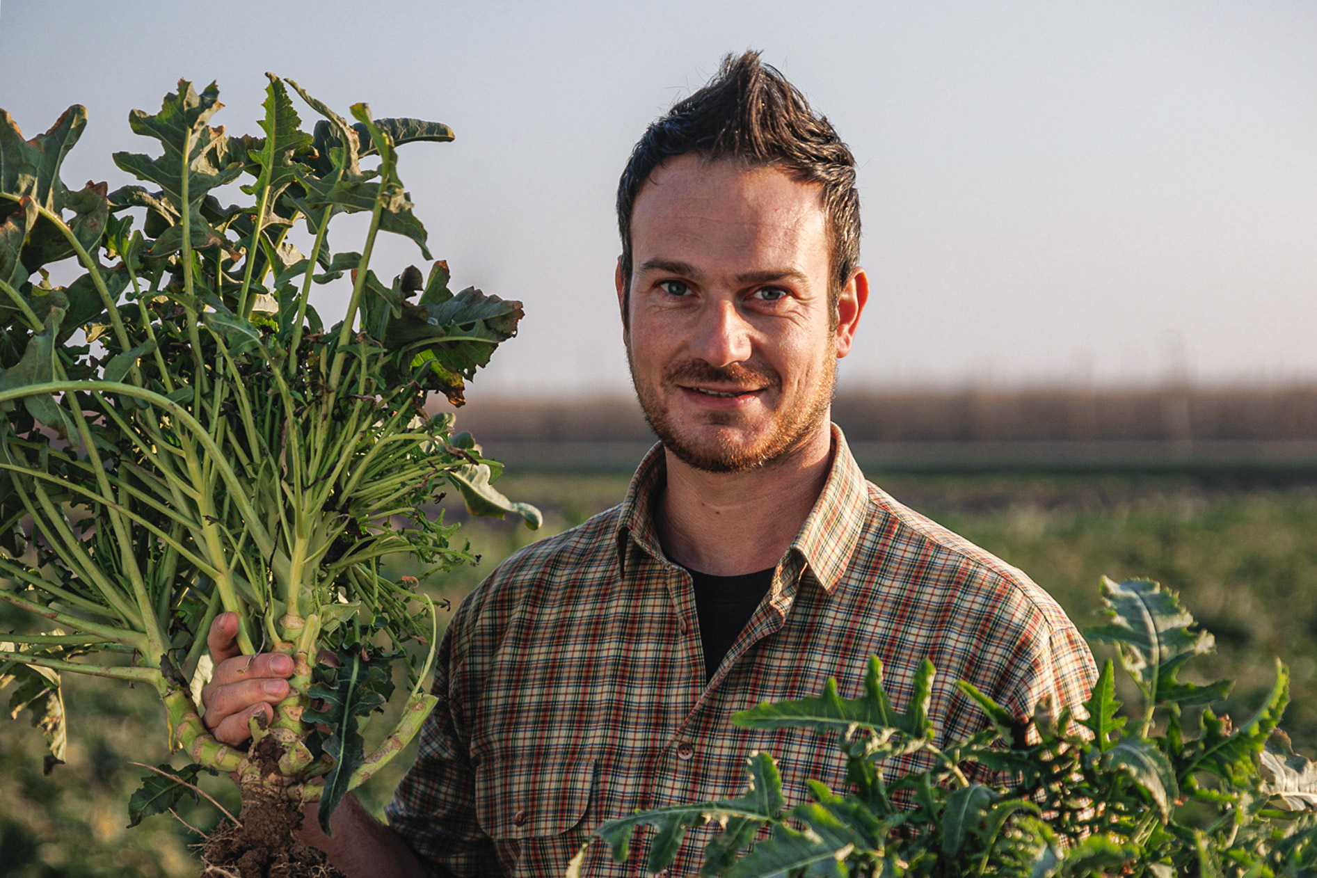 Primo piano di un giovane contadino che sorregge alcuni vegetali appena raccolti