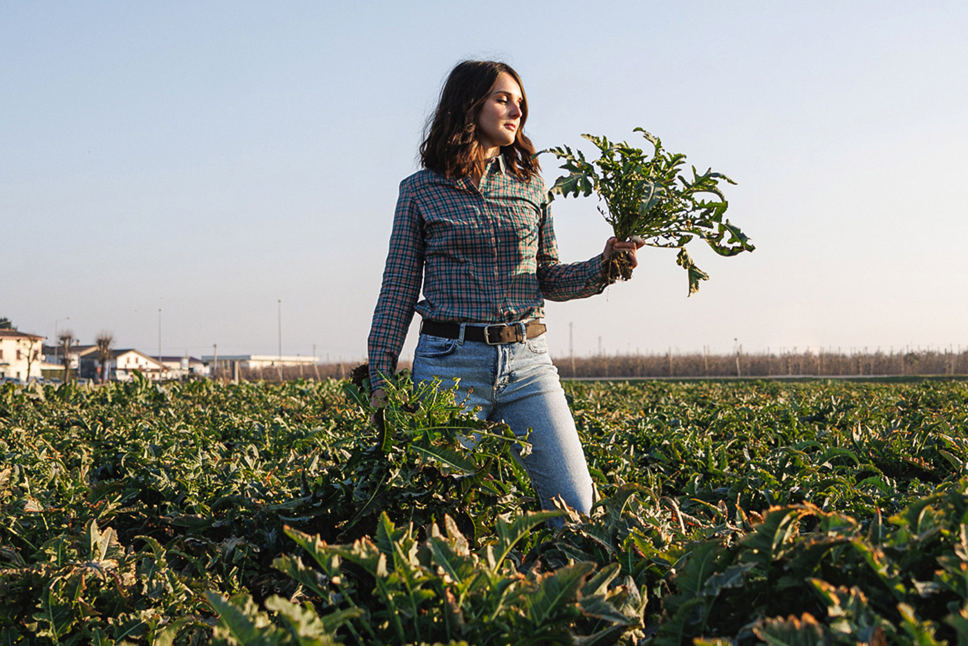 Contadina che sorregge dei vegetali appena raccolti in mezzo ai campi